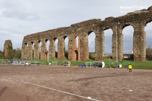 Six-storey brick arches of the Aqua Claudia rising above grassy path in Rome