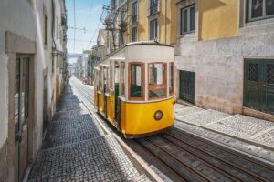 Yellow historic tram-style funicular climbs narrow Bica street in Lisbon