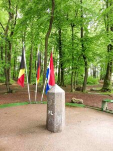 Tourists standing on a circular stone marking the Dutch-Belgian-German tripoint at Vaalserberg