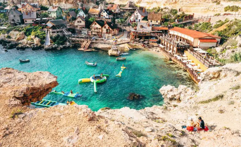 Colorful wooden buildings of Popeye Village film set beside turquoise Maltese cove