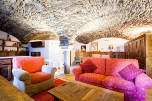 Coworking lounge with panoramic glass walls framing Valais peaks—red chairs, wooden ceiling beams